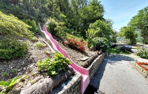 &Aacute;rea de jardim com um escorrega cor-de-rosa e plantas com flores em tempo de sol no Ristorante Albergo Grotto Serta.