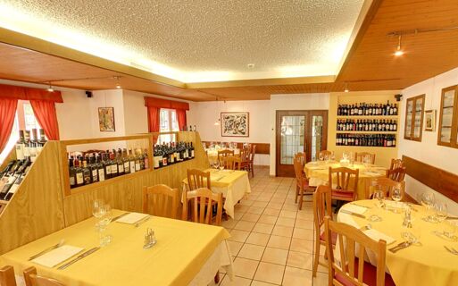 Sala de jantar acolhedora e bem iluminada, com mesas revestidas a amarelo e sele&ccedil;&atilde;o de vinhos no Ristorante Albergo Grotto Serta.