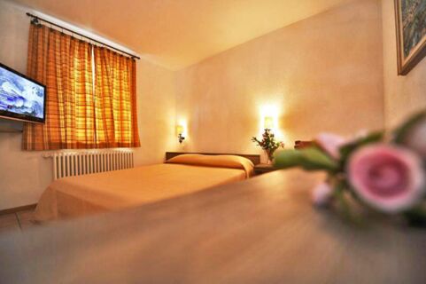 Bedroom with double bed, orange curtains, wall-mounted TV, and flowers in Ristorante Albergo Grotto Serta