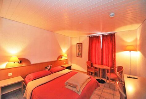 Quarto acolhedor com cama de casal, cortinas vermelhas e mobili&aacute;rio de madeira no Ristorante Albergo Grotto Serta, com uma ilumina&ccedil;&atilde;o calorosa e convidativa.