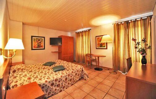 Hotel room with floral bedspread, two pillows, wooden furniture, curtains, two framed paintings, and a TV at Ristorante Albergo Grotto Serta