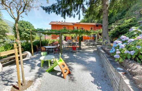 Outdoor seating area with tables and chairs under vine-covered pergolas and a small playground at Ristorante Albergo Grotto Serta
