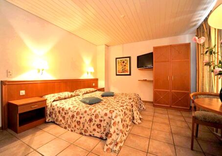 Hotel room at Ristorante Albergo Grotto Serta with twin beds covered in floral bedspreads two blue pillows on bed and wooden furniture