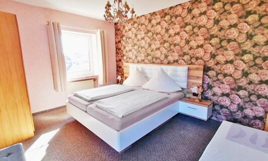 Helles Hotelzimmer mit Doppelbett und floralem Tapetendesign, gem&uuml;tlich eingerichtet im Hotel Pension Haus Hahnenbecke.