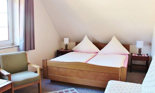 Helles und gem&uuml;tliches G&auml;stezimmer im Hotel Pension Haus Hahnenbecke mit Doppelbett, Sesseln und Nachttischen unter einem Dachschr&auml;genfenster.