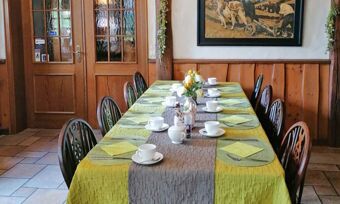 Ein gedeckter Esstisch mit gelber Tischdecke und Kaffeetassen in einem rustikal eingerichteten Raum des Hotel Pension Haus Hahnenbecke.