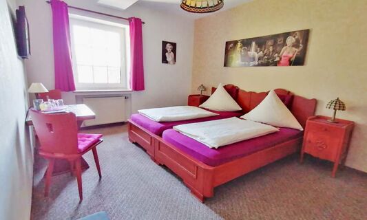 Hell eingerichtetes Doppelzimmer mit roten M&ouml;beln, violetten Bettauflagen und Fenster mit Vorh&auml;ngen im Hotel Pension Haus Hahnenbecke.