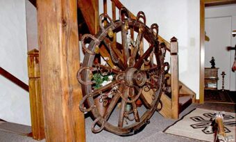 Im Inneren des Hotel Pension Haus Hahnenbecke ist ein gro&szlig;er rustikaler Holzrad-Dekorationsgegenstand neben einer Holztreppe in einem Flurbereich zu sehen.