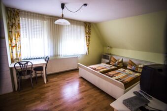 Gem&uuml;tliches G&auml;stezimmer mit Doppelbett, kleiner Sitzecke und hellem Fenster im Lindensch&auml;nke Hotel garni mit Holzboden und schr&auml;ger Decke.