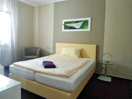 Helles, modern eingerichtetes Schlafzimmer mit Doppelbett und Sitzgelegenheit im Hotel-G&auml;stehaus Br&uuml;ggemann, schlicht und komfortabel.