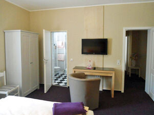 Helles G&auml;stezimmer mit Fernseher, Schrank und offenem Bad mit Kacheln im Hotel-G&auml;stehaus Br&uuml;ggemann, gem&uuml;tlich und funktional eingerichtet.