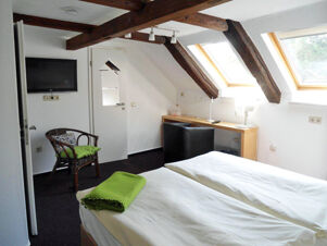 Helles Hotelzimmer mit zwei Einzelbetten, Dachschr&auml;gen mit Holzbalken und Fenstern im Hotel-G&auml;stehaus Br&uuml;ggemann, gem&uuml;tlich und funktional eingerichtet.