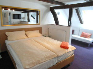 Gem&uuml;tliches Hotelzimmer mit Doppelbett, Spiegel, Sitzecke und sichtbaren Holzbalken im Hotel-G&auml;stehaus Br&uuml;ggemann.