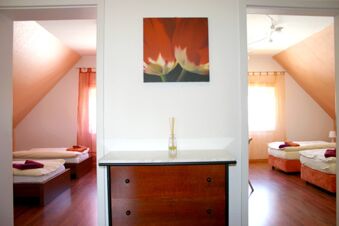 Zwei nebeneinanderliegende Schlafzimmer mit Einzelbetten, Holzfu&szlig;boden und warmem Licht im Hotel-G&auml;stehaus Br&uuml;ggemann.