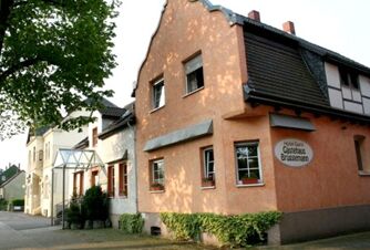 Die orangefarbene Fassade des Hotel-G&auml;stehaus Br&uuml;ggemann mit angrenzenden H&auml;usern und einem Baum im Vordergrund bei Tageslicht.