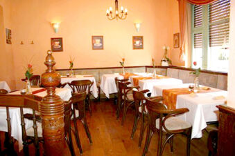 Gem&uuml;tlicher Restaurantbereich im Hotel-G&auml;stehaus Br&uuml;ggemann mit mehreren Tischen, wei&szlig;en Tischdecken und Holzst&uuml;hlen in warmem Licht.