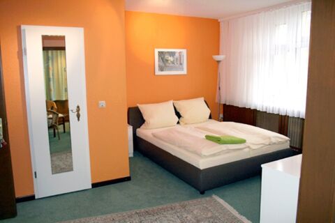 Gem&uuml;tliches Zimmer im Hotel-G&auml;stehaus Br&uuml;ggemann mit Doppelbett, orangen W&auml;nden, gro&szlig;em Fenster und schlichtem Mobiliar f&uuml;r G&auml;ste.
