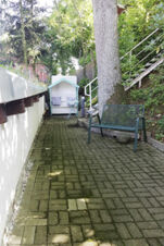 Schattiger Gartenweg mit gepflastertem Boden, Metallbank und einem wei&szlig;en Strandkorb im Landhotel Alte M&uuml;hle, umgeben von B&auml;umen und Gr&uuml;n.