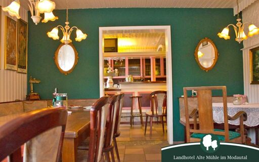 Gem&uuml;tlicher Speiseraum mit Holzm&ouml;beln, gr&uuml;nen W&auml;nden und dekorativen Spiegeln im Landhotel Alte M&uuml;hle mit Blick in die Bar.