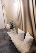 Ein gem&uuml;tlicher Flur im Landhotel Alte M&uuml;hle mit einer Bank, weichen Kissen und einer Vase mit Blumen vor einer Wand mit Holzlamellen.