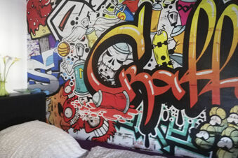 Bunt gestaltetes Zimmer mit Graffiti-Wandkunst im Landhotel Alte M&uuml;hle, kreative und moderne Atmosph&auml;re im Schlafbereich.