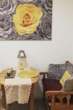 Gem&uuml;tliche Sitzecke mit Holztisch, Kissen und dekorativem Bild mit gelber Rose im Landhotel Alte M&uuml;hle f&uuml;r entspannte Momente.