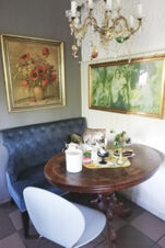 Gem&uuml;tliche Sitzecke mit blauem Polstersofa, ovalem Holztisch und kunstvollen Bildern in Landhotel Alte M&uuml;hle, perfekt f&uuml;r entspannte Momente.