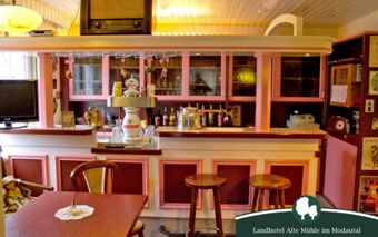 Gem&uuml;tliche Bar mit Holztheke und Hockern im Landhotel Alte M&uuml;hle, dekoriert mit klassischen M&ouml;beln und stilvollem Ambiente.