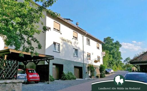 Au&szlig;enansicht des Landhotel Alte M&uuml;hle mit Parkpl&auml;tzen und B&auml;umen an einem sonnigen Tag im Modautal.